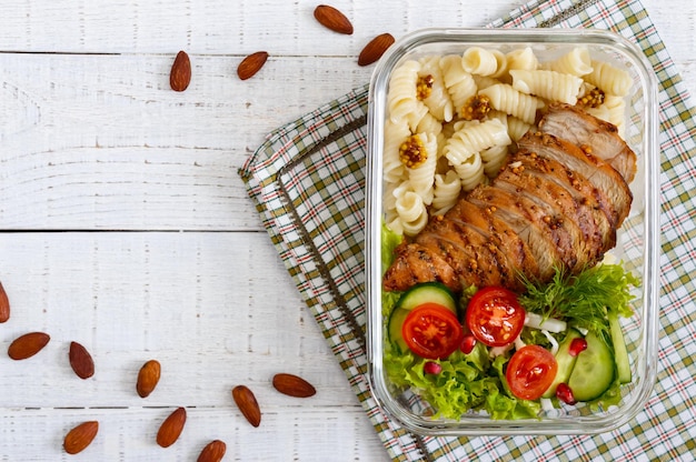 Lunch box: rotini with baked chicken breast and salad on a white wooden background. Top view, flat lay. Delicious healthy lunch. The concept of healthy eating.