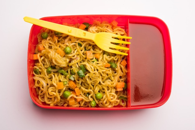 Lunch Box or Tiffin for Indian kids, contains hot noodles with fresh vegetables along with tomato ketchup. selective focus