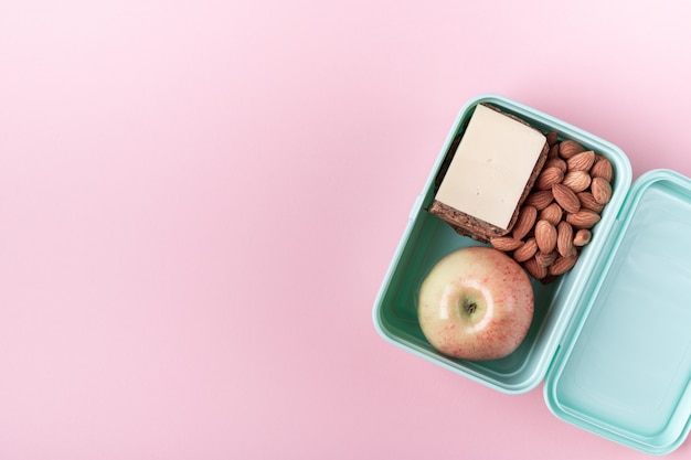 Lunch box with apple, sandwich and almond on pink 