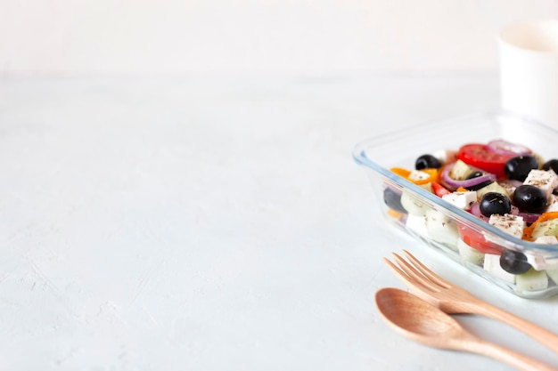 Ланч-бокс с греческим салатом, многоразовая стеклянная тара, деревянные столовые приборы, на белом фоне, копировальное пространство