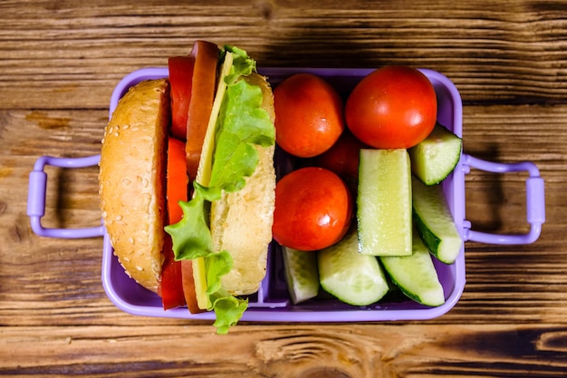 Lunch box with hamburger cucumbers and tomatoes on rustic wooden table Top view