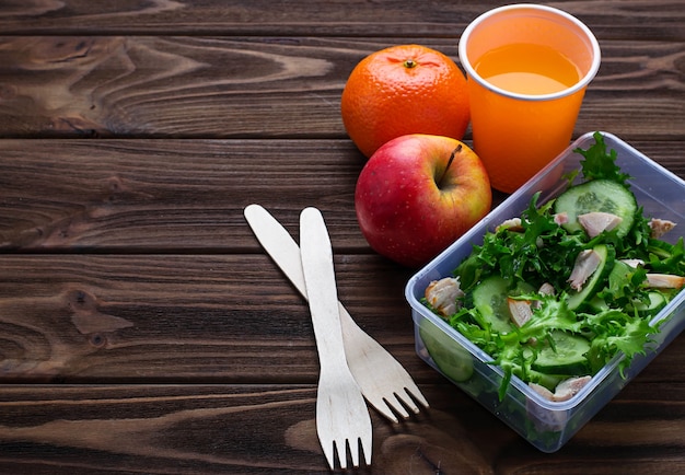 Lunch box with salad, apple, tangerine and juice. 