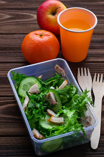 Lunch box with salad, apple, tangerine and juice. 