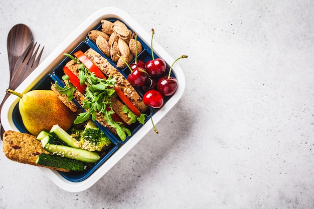 Lunch box with sandwich, pear, vegetables, nuts and snacks on gray 