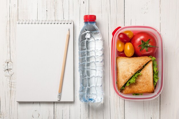 Lunch box with sandwich and tomatoes, bottle of water and notepad