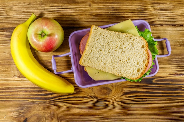 Lunch box with sandwiches banana and apple on a wooden table Top view