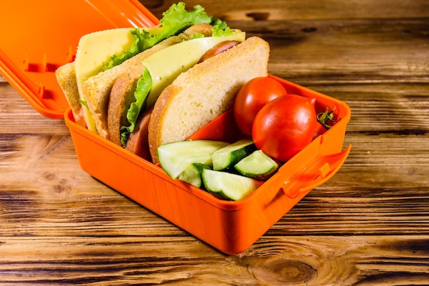 Photo lunch box with sandwiches cucumbers and tomatoes on rustic wooden table