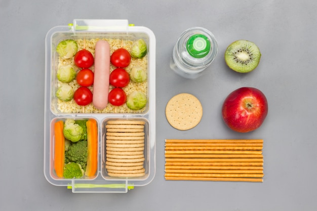 Lunch box with sausage, broccoli and tomatoes.