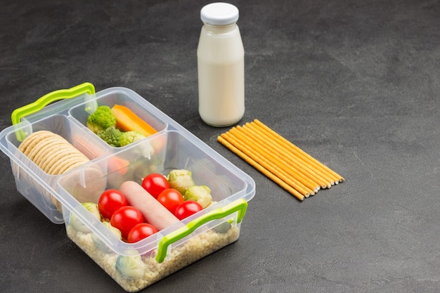 Lunch box with sausage and vegetables, bottle of yogurt and edible straws