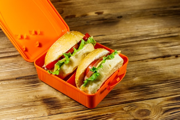 Lunch box with two homemade cheeseburgers on wooden table