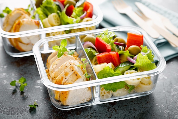 Lunch boxes with grilled chicken breast and pasta salad with fresh vegetables