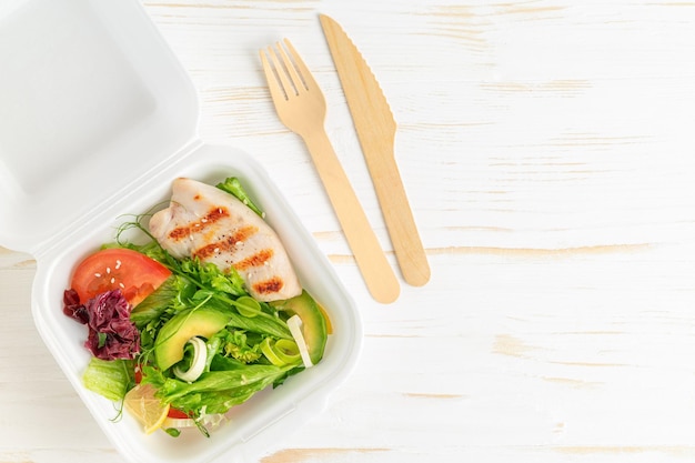 Lunch boxes with salad and grilled chicken on white wooden background Top view