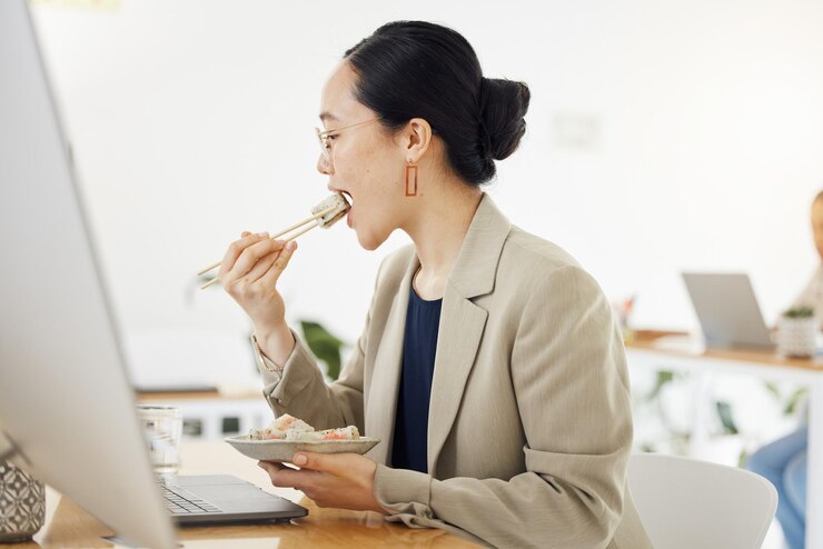 Photo ランチブレイク 食事とビジネス 女性 オフィスデスクで食事 電子メールやプロポーズのラップトップを読みながら 寿司 ブランチと空腹のデザイナー 効率的な生産性と時間管理のためのテイクエイ