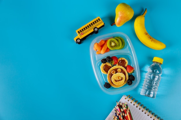 Lunch container with pancakes, carrot, pear and banana with scool supplies. Back to school concept.