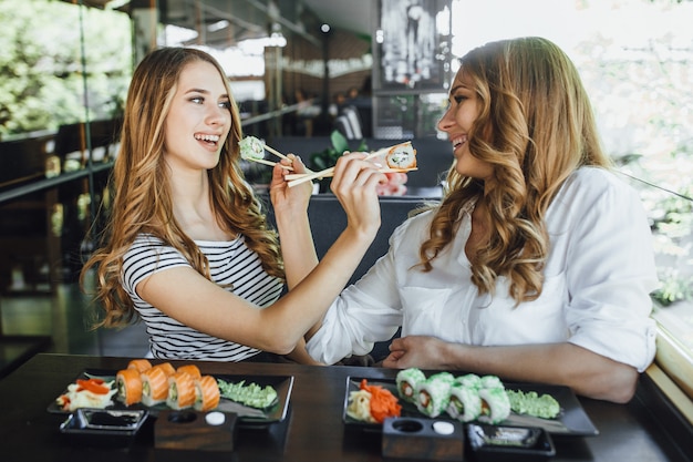 Lunch in een chinees restaurant op het zomerterras. moeder en haar jonge mooie dochter eten sushi met chinese stokken