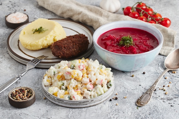 Lunch in kom en borden met vork en lepel, keukendoek en tomaten op lichte marmeren achtergrond