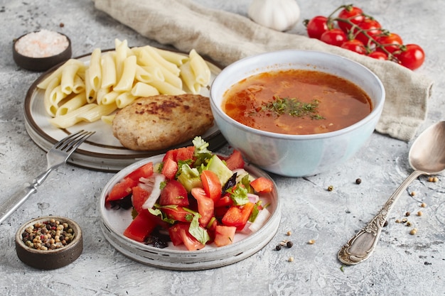 Lunch in kom en borden met vork en lepel, keukendoek en tomaten op lichte marmeren achtergrond