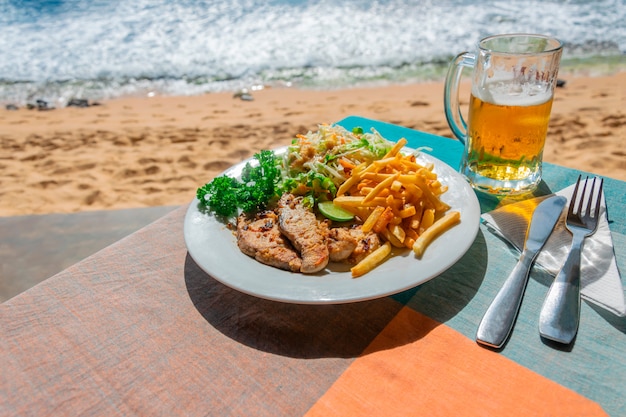 Foto pranzo in un bar all'aperto sul mare o sull'oceano. fette di pesce fritto e patatine fritte con insalata di cavolo e un bicchiere di birra chiara fredda