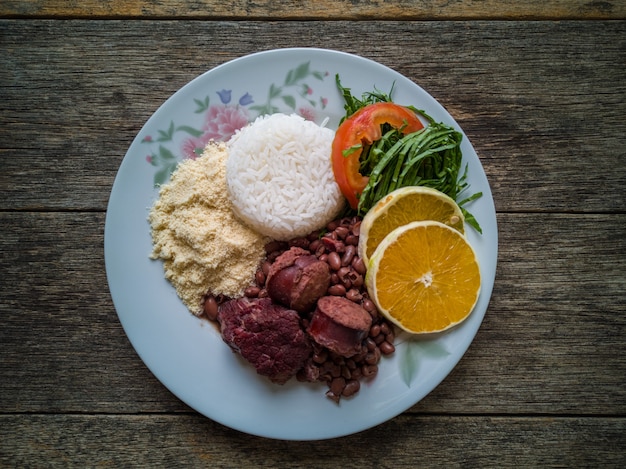 Lunch plate with traditional Brazilian feijoada and wooden background.