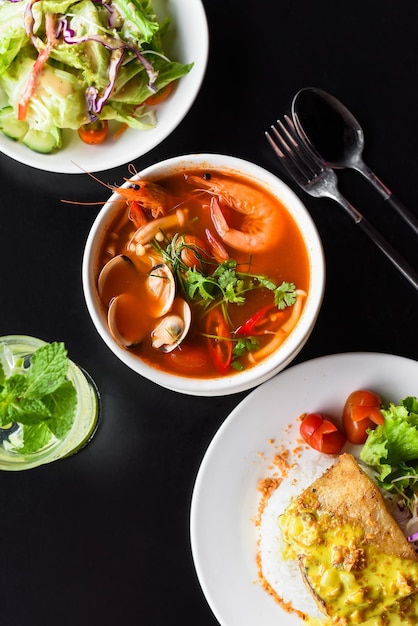 Обеденный набор из супа том ям, салата, жареной рыбы баса, риса, на черном фоне