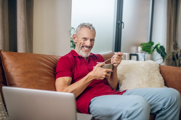 Photo lunch time. grey-haired man having lunch and watching a video