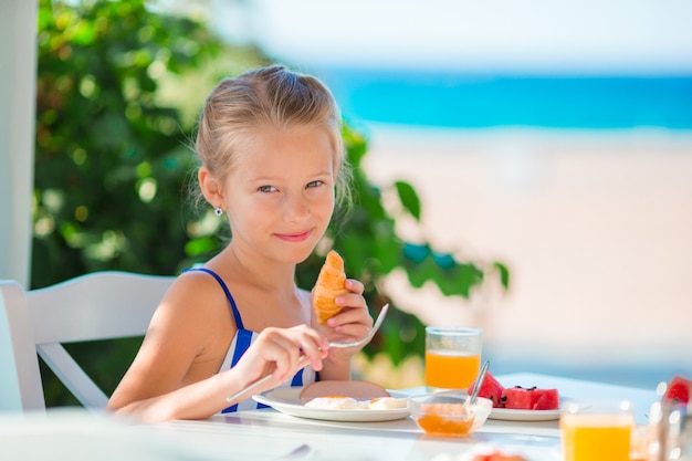 ランチタイム。海の景色と屋外カフェで朝食を持っている少女