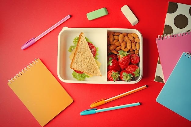 Lunchbox met eten en briefpapier op rode achtergrond bovenaanzicht