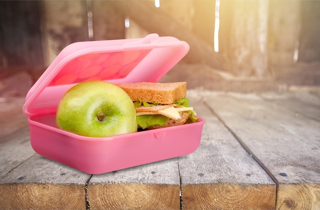 Photo lunchbox with an apple and sandwich on table