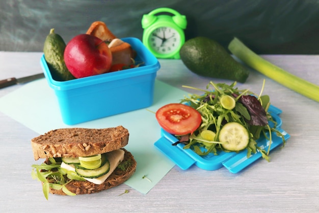 Lunchbox with cereal bread sandwich with cheese organic vegetables and micro greens apple