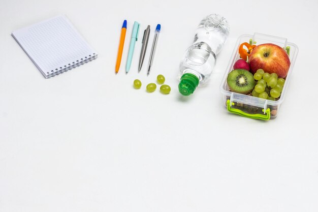 Lunchbox with fruits on table Notepad Pens headphones and bottle of water