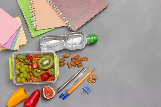 Lunchbox with nuts and fruits and Pens and notebooks, flat lay