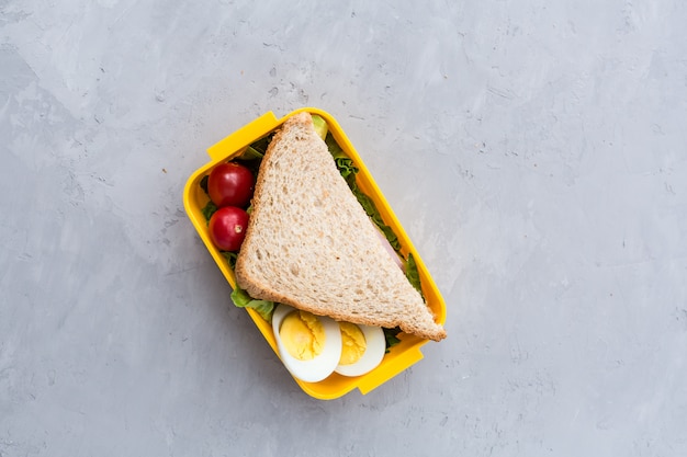 Lunchbox with sandwich and different products on gray