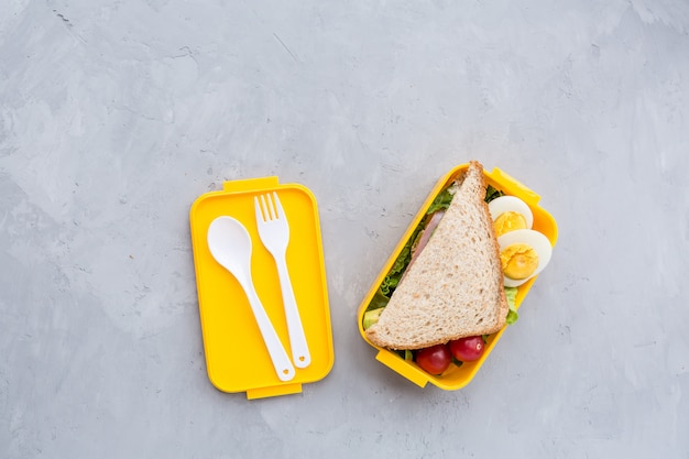 Lunchbox with sandwich and different products on gray 