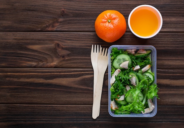 Lunchdoos met salade, appel, mandarijn en sap.