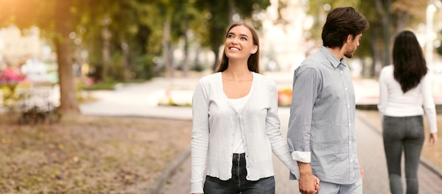 Lustful cheating boyfriend looking at other woman walking with girlfriend in park outdoors selective