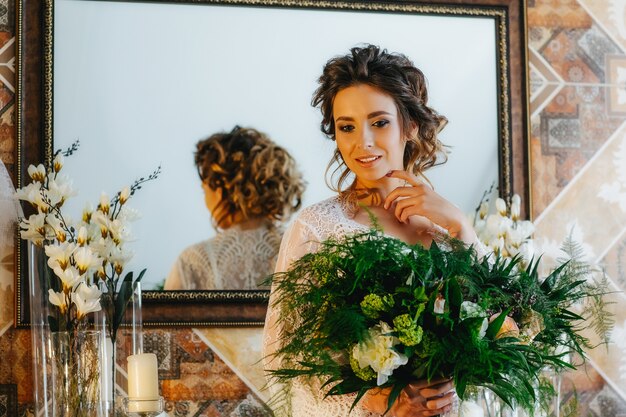 Luxe bruid in een prachtig kanten gewaad met een boeket bloemen en groen