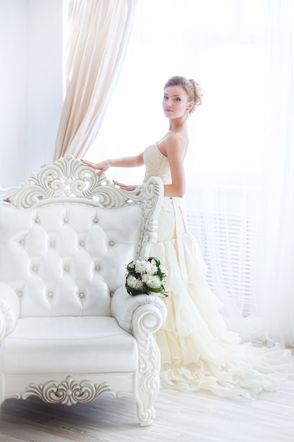 Luxe bruid moet zich kleden voor het raam op een lichte achtergrond.