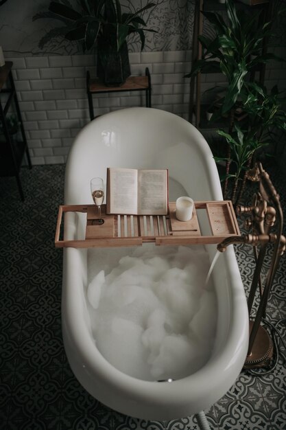 Luxe interieur van moderne badkamer in ecostijl met ovaal bad en boek op bamboehouten dienblad