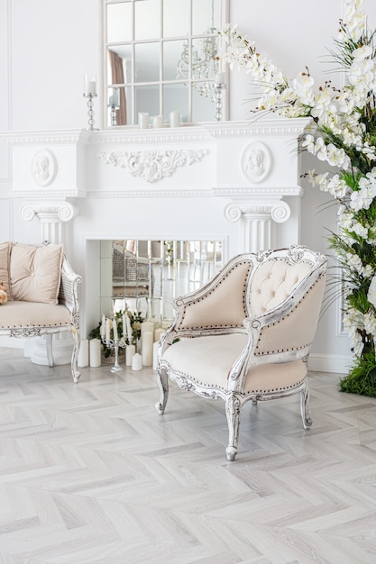 Luxe lichte ruime logeerkamer met mooie chique meubels een enorm raam van vloer tot plafond in koninklijke stijl is versierd met groene planten, witte muren met stucwerk en een open haard