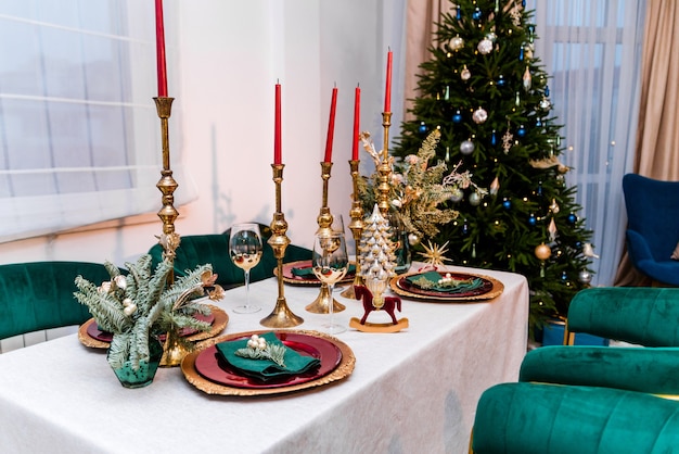 Luxe Nieuwjaar interieur van de kamer. De kamer bevat een kerstboom, corduroy fauteuils en een grote tafel. Op de tafel staan gouden borden, kaarsen en nieuwjaarsdecoratie. Foto