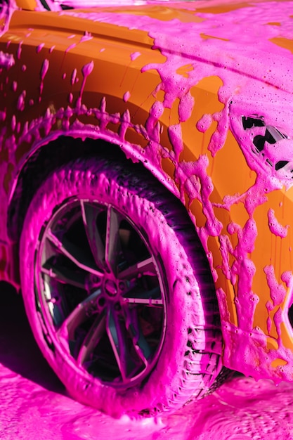 Luxe oranje auto op zelfbediening auto wassen roze schuim op auto close-up van wielen