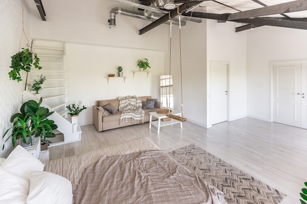 Foto luxe slaapkamerontwerp in een rustiek huisje in een minimalistische stijl. witte muren, panoramische ramen, houten decoratie-elementen aan het plafond, touwschommels in het midden van een ruime kamer.