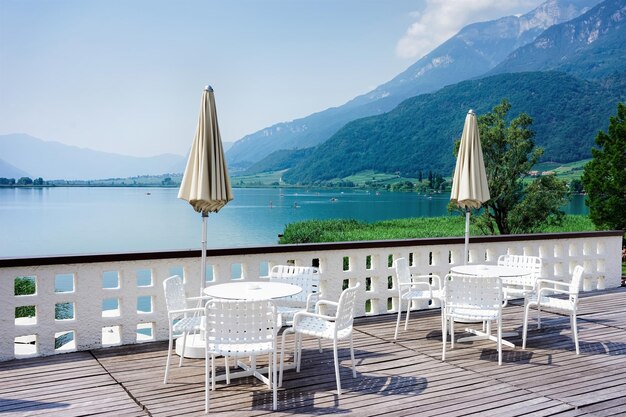 Luxe straatrestaurant aan het Caldaro-meer in Zuid-Tirol, Italië. Italiaans terras met tafels en stoelen en parasols bij Kalterer See. Lifestyle terras ontwerp en concept. Uitzicht op het meer in de zomer.