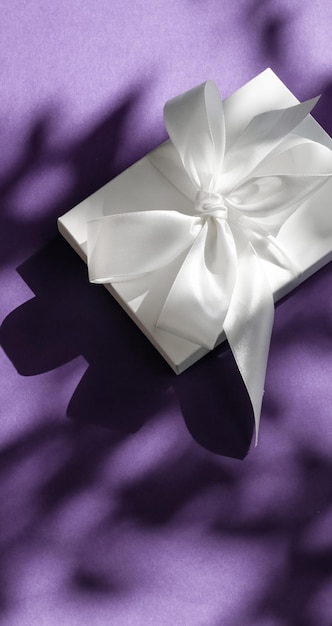 Luxe vakantie witte geschenkdoos met zijden lint en strik op violette achtergrond luxe bruiloft of verjaardagscadeau