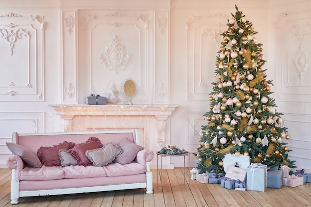 Luxe woonkamer interieur met sofa versierde chique kerstboom, geschenken en kussens. Klassiek interieur in roze tinten. Kerst thuis.