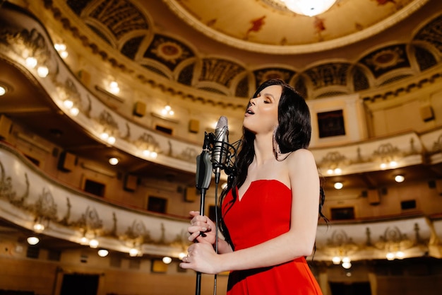 A luxurious actress in a red dress sings on stage with a microphone in her hands