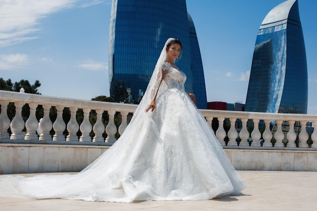 A luxurious bride in a tight wedding dress is standing in a park with a flying veil