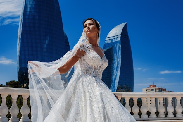 A luxurious bride in a tight wedding dress is standing in a park with a flying veil