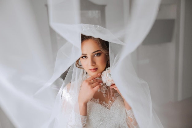 A luxurious bride with a beautiful hairstyle and a gorgeous dress is getting ready for the wedding ceremony in the morning Morning photo of the bride at home or in a hotel room Professional makeup