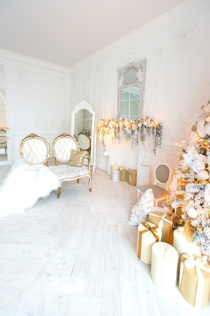 Luxurious expensive light interior living room in a royal style decorated with a Christmas tree and large windows